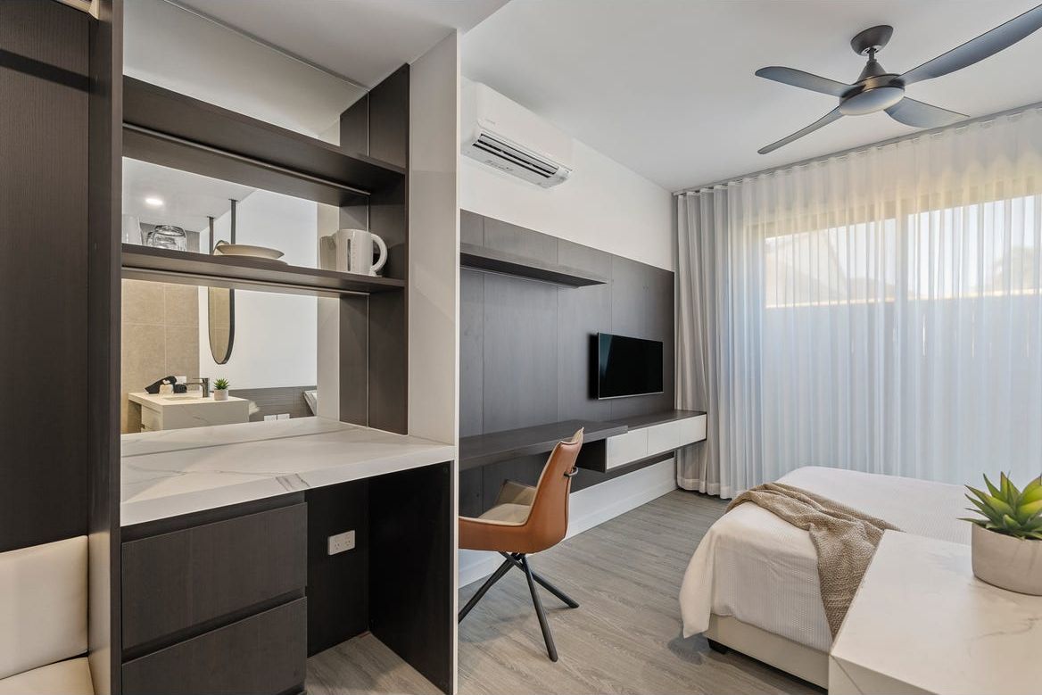 Harmony co-living suite with a study desk, wall-mounted TV and sheer curtains